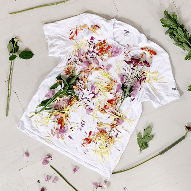 White t shirt laid out with flowers and greens laying on it. 